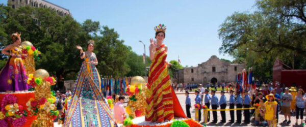 Three women waving to the crowd at the Flower Parade in front of the alamo