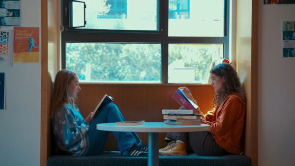 Film still of two students sitting at a bench in a window reading