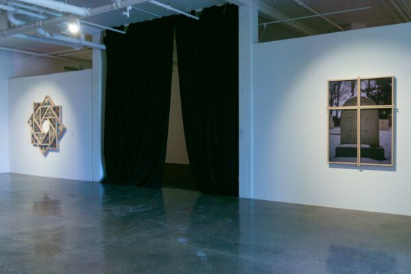 Installation view of photos on either side of a dark curtain