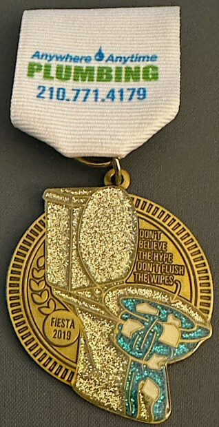 Fiesta medal by a plumbing company with a gold glittery toilet