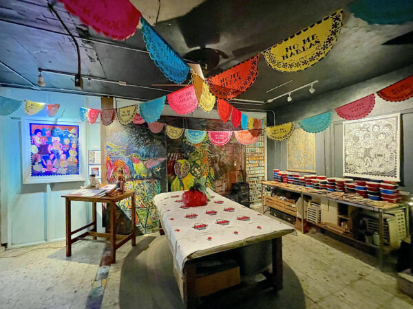 Photo of an installation with papel picado, large figurative paintings, and prints