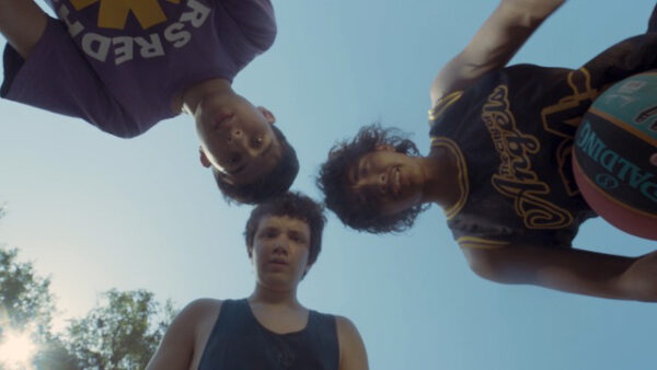 Film still of three teenage boys playing basketball looking into camera