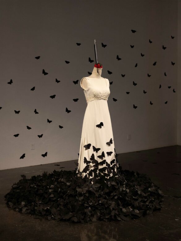 Installation of a white wedding dress semi covered with black butterflies