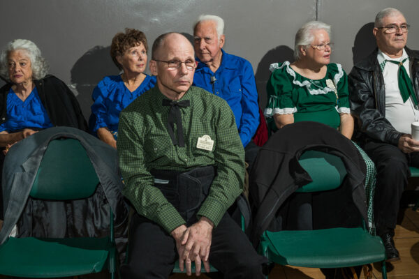 Photo of elderly people wearing green and blue sitting in chairs