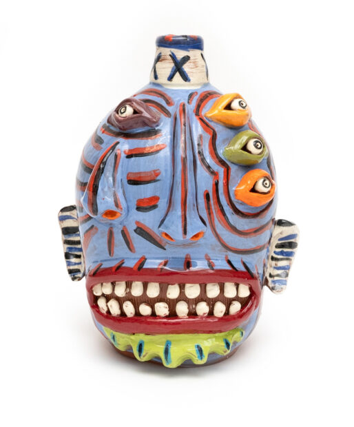 A ceramic jug featuring a distorted face with multiple eyes, a nose, and a large mouth.