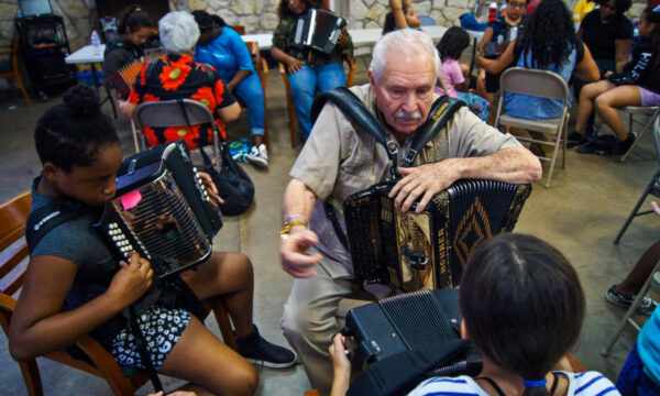 A photograph of a man teaching children how to play the accordion. 