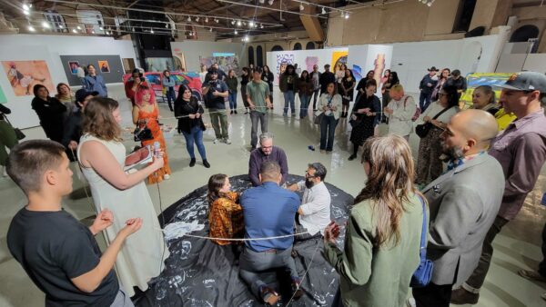 Photo of performance participants in a circle with visitors watching
