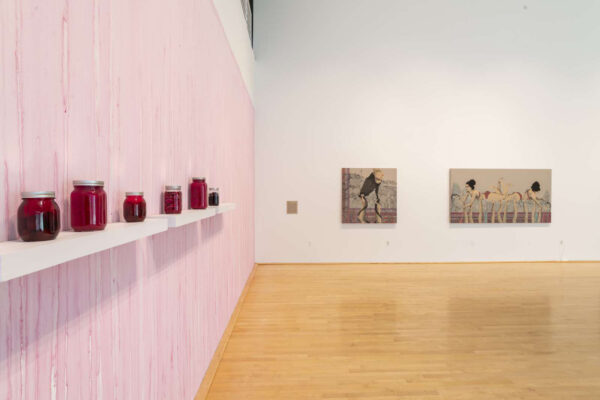 Installation view of red jars against a pink wall and two paintings