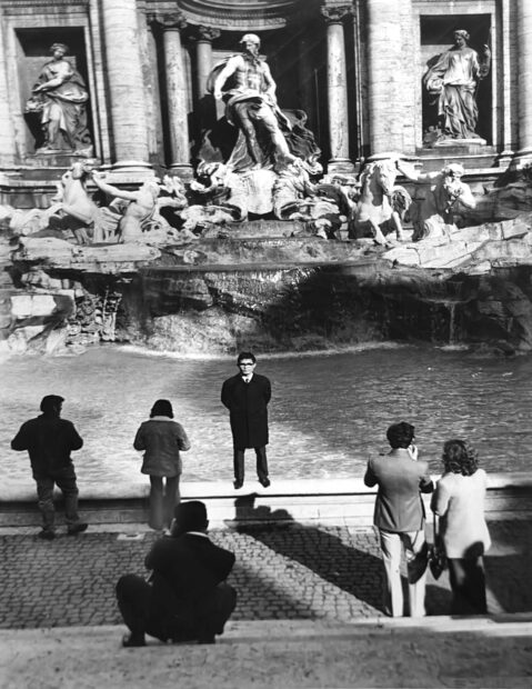 A man stands before the Trevi Fountain posing for a photograph.