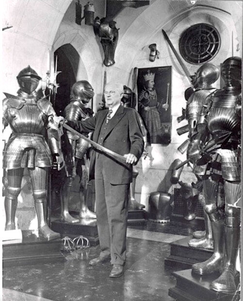 Black and white photo of a man holding a sword surrounded by armor