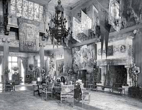 Photo of an interior with many draping tapestries, flags, armor, chairs, and a large fireplace