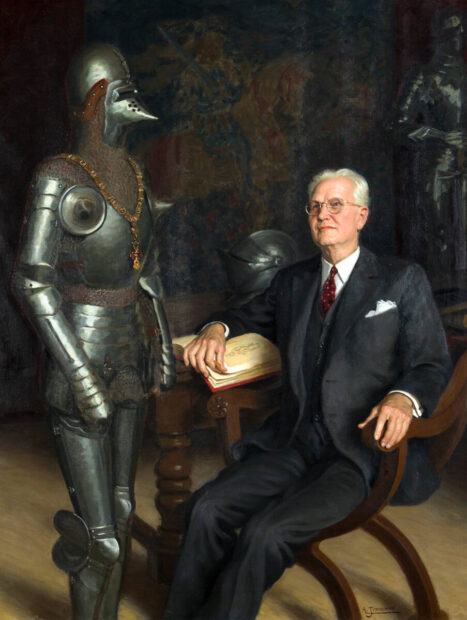 Portrait of an older white man next to a suit of armor