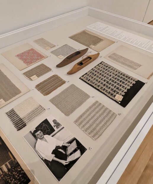 A display case containing fabric samples, loom pieces, small weavings, and a black and white phot of Anni Albers.