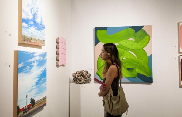 View of a visitor looking at landscape paintings on a wall at the affordable art fair