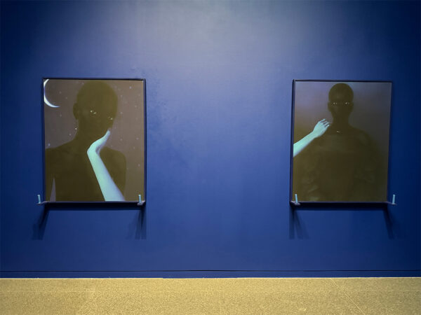 An installation image of two photographs by Elliot and Erick Jiménez in a blue room. 