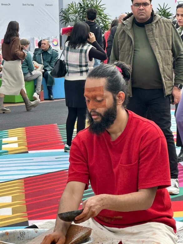 A seated man mixes pigments during a performance.