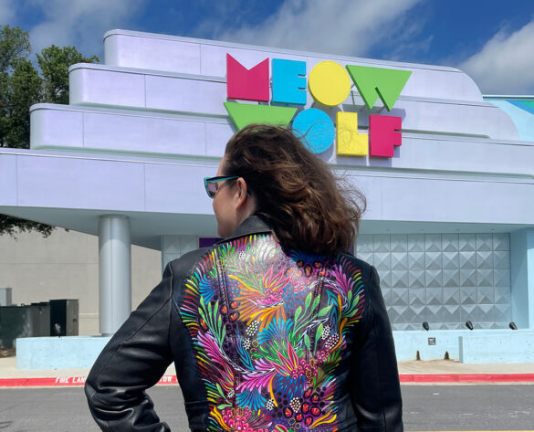A photograph of artist Lauren Lewchuk in front of the Meow Wolf Grapevine location.