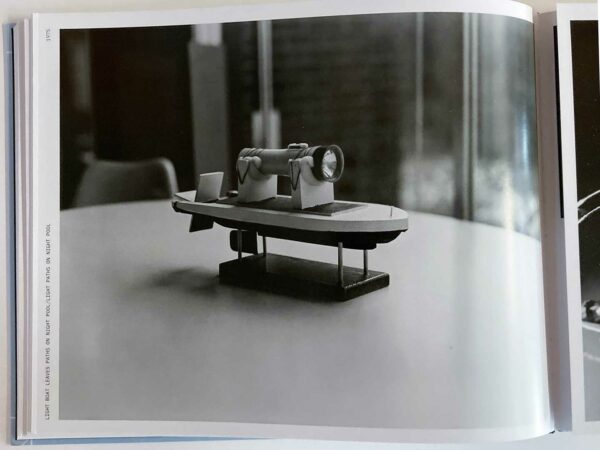A small toy boat with a flashlight attached to it sits atop a table in a black and white photograph.