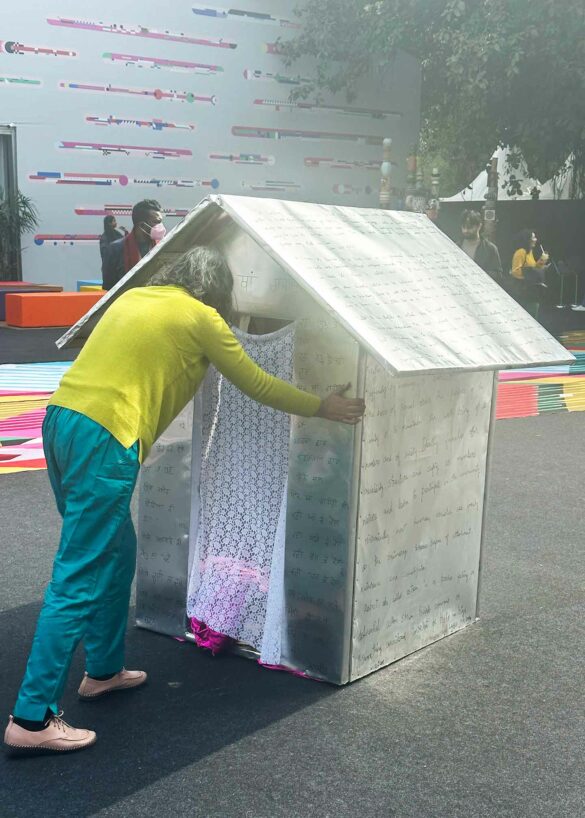 A woman pushes a small sculpture of a home across the pavement in an art performance.