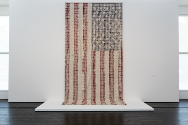 A photograph of a work of art by Nari Ward featuring U.S. flag with 6,000 white plastic security tags.