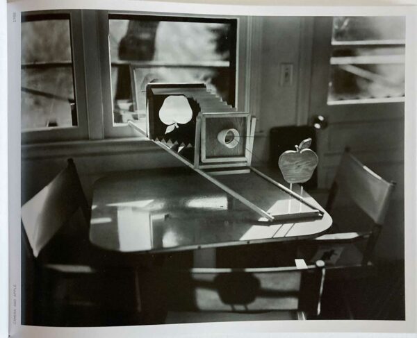 A camera is propped up on a table with its lens aimed at a wooden cut out of an apple