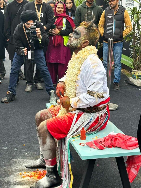 A man sits on a bench during a performance with his face painted.