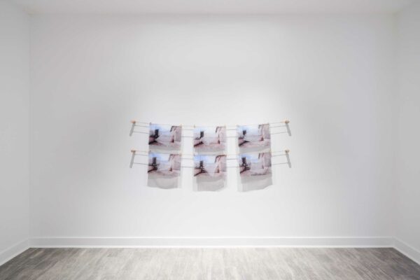 Six images printed on translucent fabric hang on clotheslines on the walls of a gallery.