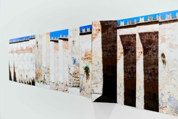 A long, unframed photograph of an Italian wall along the via Cavour hangs on the wall of a gallery.