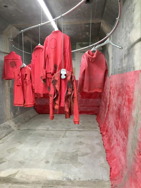 Red rubber jackets hang in a concrete space with red rubber casting on the wall to the right. 