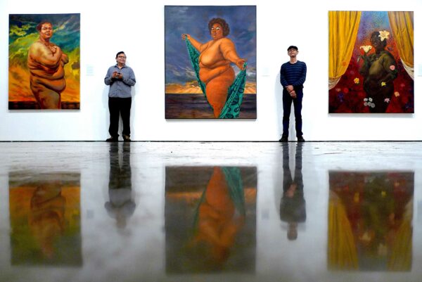 Photo of two artists standing between three large paintings
