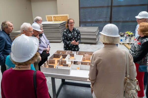 A photograph of curator Maggie Adler speaking with a group of people on a tour of a gallery under renovation.
