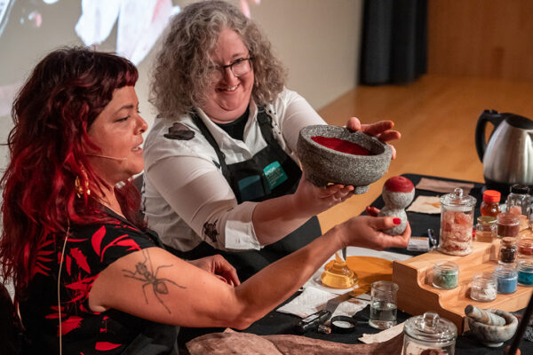 A photograph of artist Sandy Rodriguez and curator Maggie Adler discussing paint pigments.