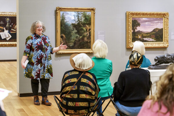 A photograph of curator Maggie Adler speaking to a group about a painting in the Amon Carter Museum's permanent collection. 
