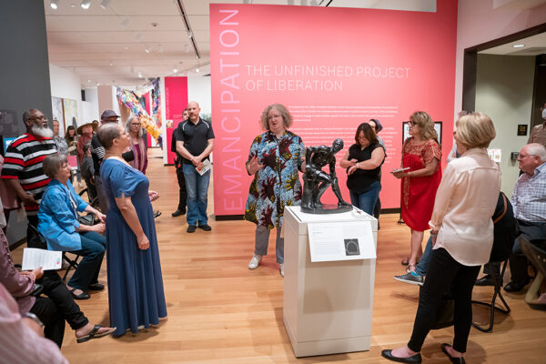 A photograph of curator Maggie Adler leading a tour through an exhibition.