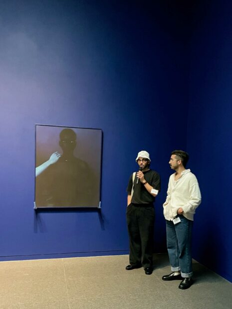 Photo of two artists speaking on their work in a gallery with blue walls