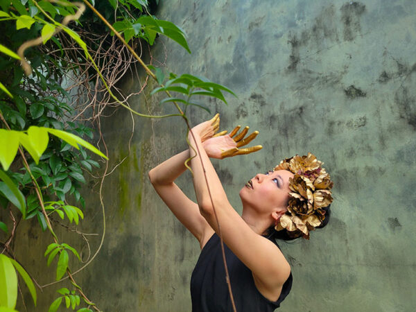 A dancer in a black dress performs outdoors with a laurel wreath on her head.