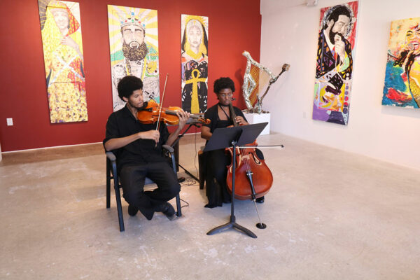Two musicians perform in a gallery. One plays a viola and the other plays a cello.