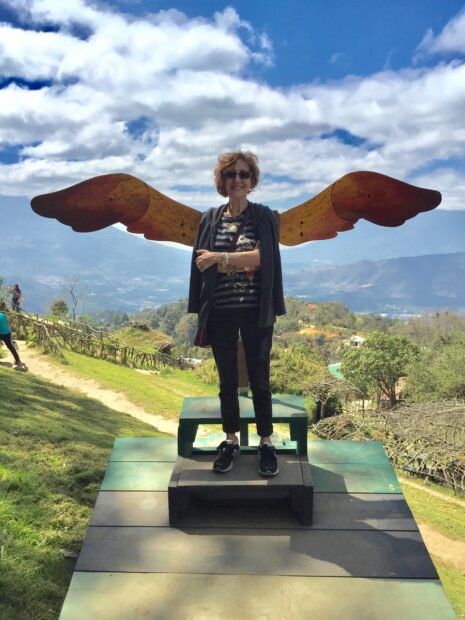 A photograph of gallerist Anya Tish posing in front of a sculpture with wings.