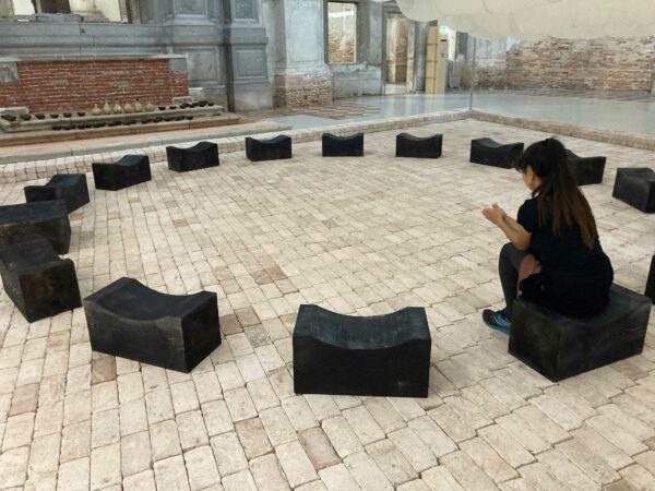 Installation view of a woman sitting on black benches in a circle