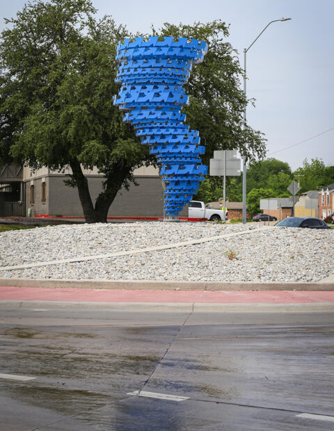 A photograph of a public art sculpture by Mark Reigelman featuring hundreds of small blue arrows that make up a spiral form.