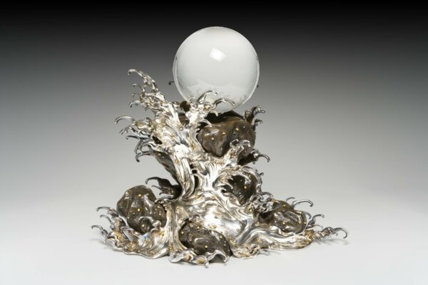 A sculpture by Yukihiro featuring a crystal sphere atop a metal wave crest.