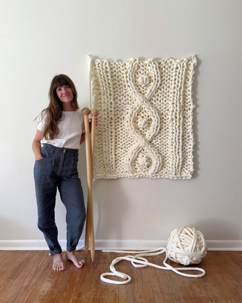 A photograph of artist Cassie Arnold standing next to a large textile work.