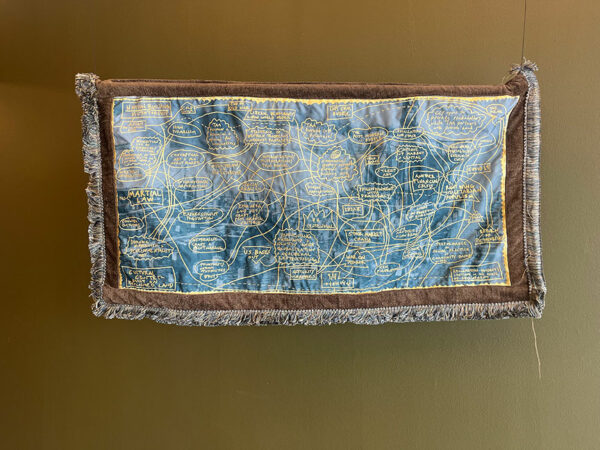 A fabric piece with embroidered words hangs on a brown wall.