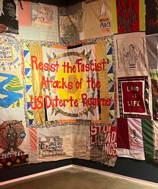 A wall of quilts with political messages are installed in the corner. 