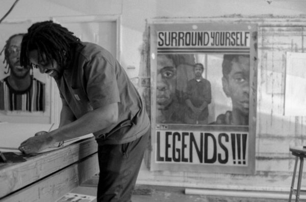 A black and white photograph of artist Riley Holloway in his studio.