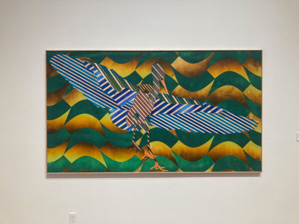 A painting constructed of individual pieces of painted wood depicts an egret in flight against a background of uniformly tiles planes