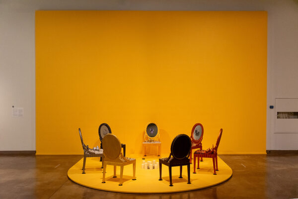 A photograph of an installation of eight modified chairs positioned in a circle. Artwork by Amalia Mesa-Bains.