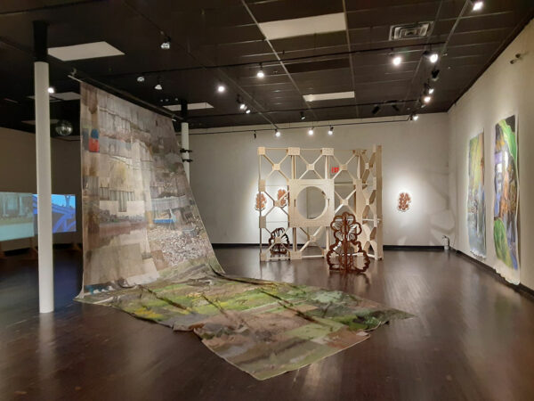 A large cloth installation fills a gallery, to its right are metal and wood sculptures.