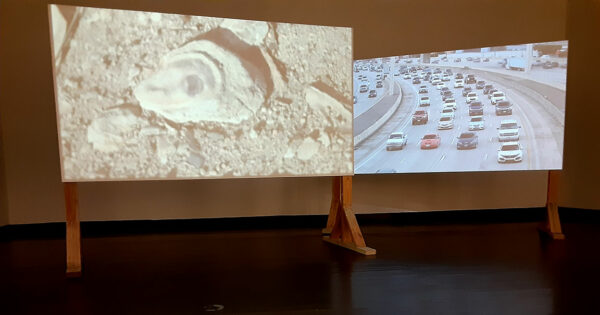 Two large wooden screens stand in a gallery with two simultaneous projections playing. 