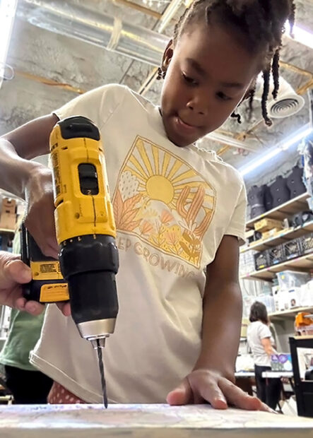 A photograph of a young girl holding a power drill.